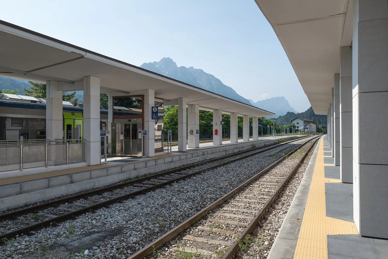 Binari e pensiline della stazione ferroviaria di Calalzo-Pieve di Cadore-Cortina in estate, con le montagne del Cadore sullo sfondo