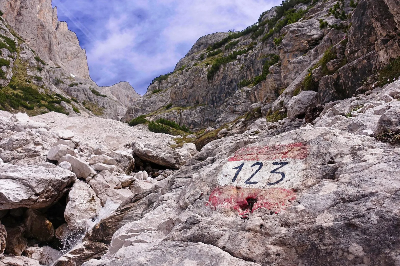 Segnavia bianco e rosso con il numero 123 dipinto su una roccia, lungo un sentiero sassoso tra pareti dolomitiche in Val d'Ambata